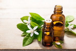 neroli essential oil in the brown glass bottle, with fresh white neroli flower and green leaves.